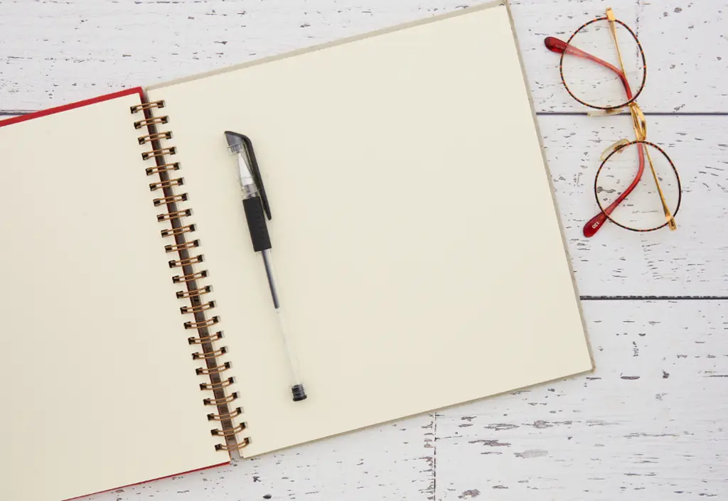 Sur une table claire, un stylo, des lunettes et un carnet ouvert
